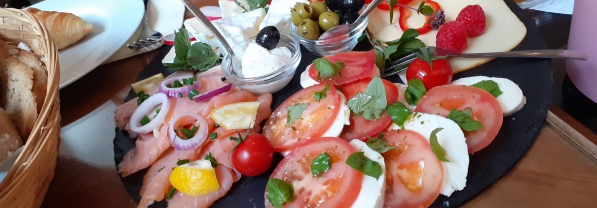 Ein Servierteller mit Lach, Tomate-Mozzarella und Käse, daneben Marmeladengläschen